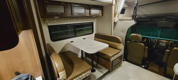 Explore this rv rental interior: a cozy dinette, ample overhead storage, and driver's cabin visible. Perfect for road trips.. Coachmen Prism 2022