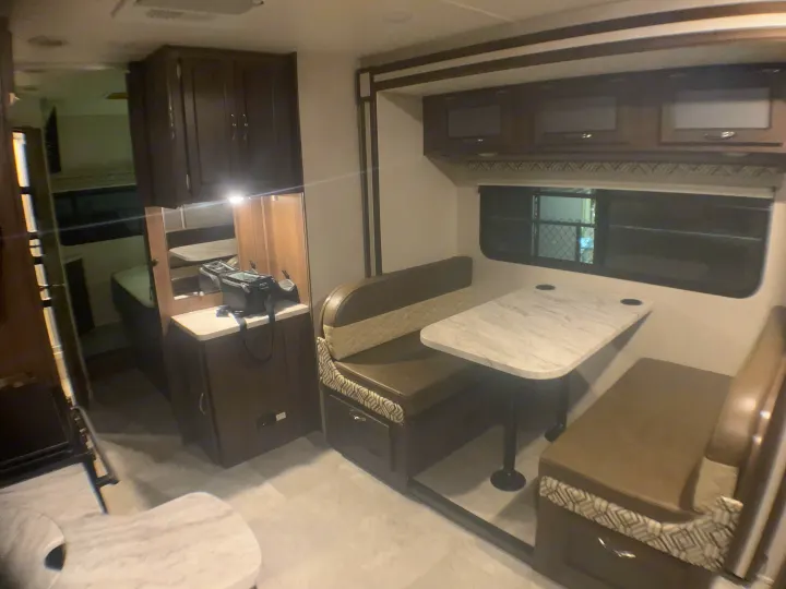 Inside this RV rental: a modern dinette with a marble-look table, ample cabinets, and a glimpse of the sleeping area.. Coachmen Prism 2022