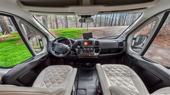 Spacious RV rental cockpit showing dashboard, steering wheel, quilted seats, and wooded view outside.. Jayco Swift 2022