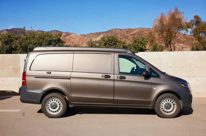 This dark brown pop-top camper van, ideal for an RV rental, is parked with a mountain backdrop under a clear blue sky.. Mercedes-Benz Metris 2018