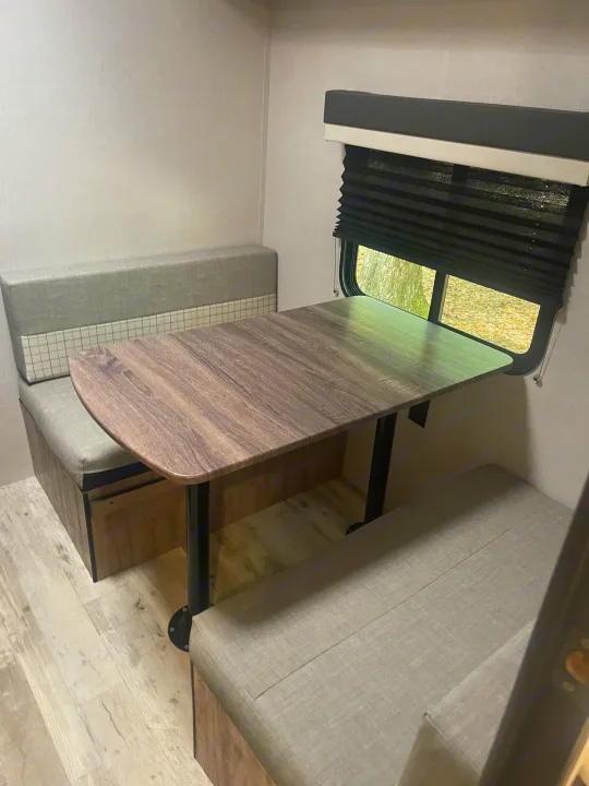 Spacious RV rental dinette with wood-look table and comfy grey upholstered benches. Ideal for meals on the go.. Gulf Stream Innsbruck 2023