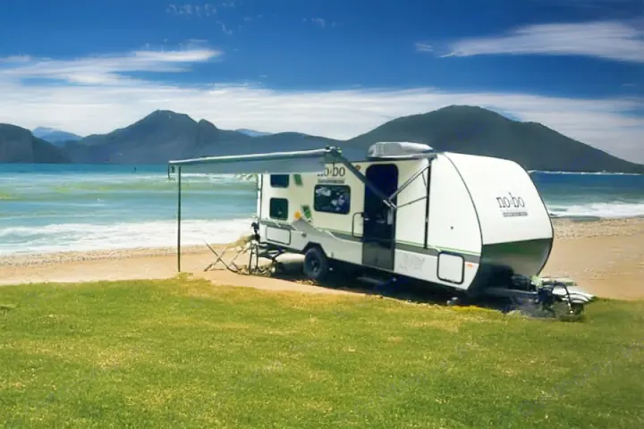 Enjoy an rv rental by the sea! This travel trailer with an extended awning is set on a grassy beach campsite, facing mountains.. No Boundaries NoBo 19.3 Essentials Only 2024
