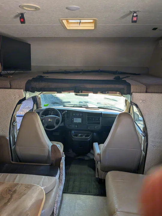 RV rental interior: spacious front cabin with dashboard, comfy driver/passenger seats, and an overhead bunk bed.. Coachmen Freelander 2018