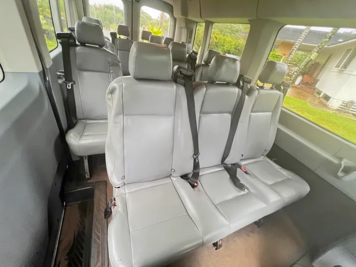Spacious vehicle interior, often seen in rv rentals, showing multiple rows of grey seats and seatbelts with outside views.. Ford Custom Transit 2016