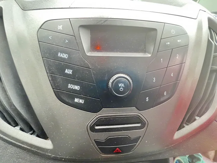 RV rental's dusty car radio console: media controls (radio, AUX, sound), volume knob, preset buttons, and hazard light button.. Ford Custom Transit 2016