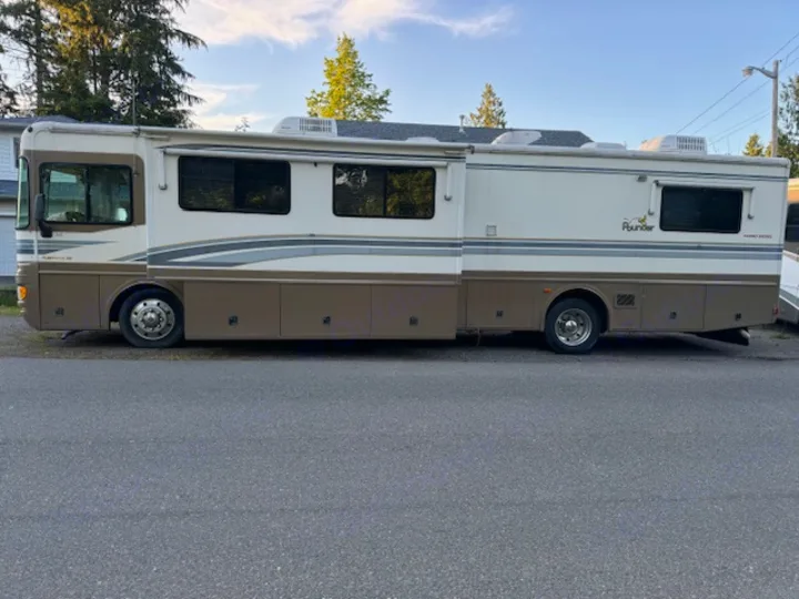 Side view of a large cream & brown Fleetwood Bounder motorhome, an ideal RV rental for road trips. Parked on asphalt.. Fleetwood 39/MH 2000