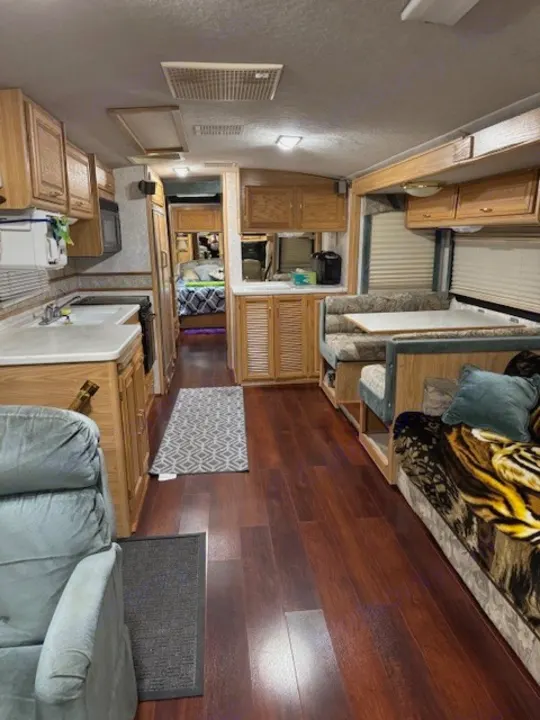 Spacious RV rental interior featuring a full kitchen, comfortable living/dining areas, and a visible bedroom, ideal for travel.. Fleetwood 39/MH 2000