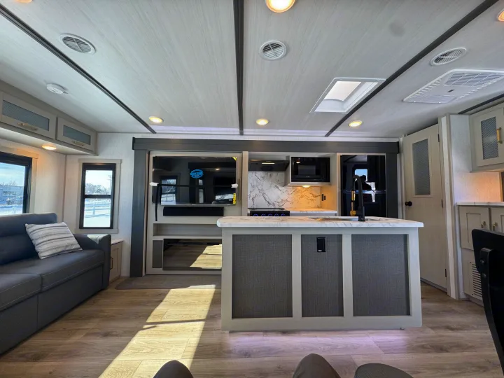 Inside a bright RV rental: modern kitchen island, cozy sofa, TV, and snowy landscape outside the window.. Forest River Salem Hemisphere 2024