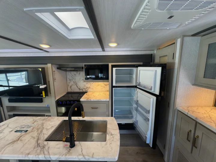 Spacious RV rental kitchen with modern appliances: open fridge, stove, microwave, and island sink.. Forest River Salem Hemisphere 2024