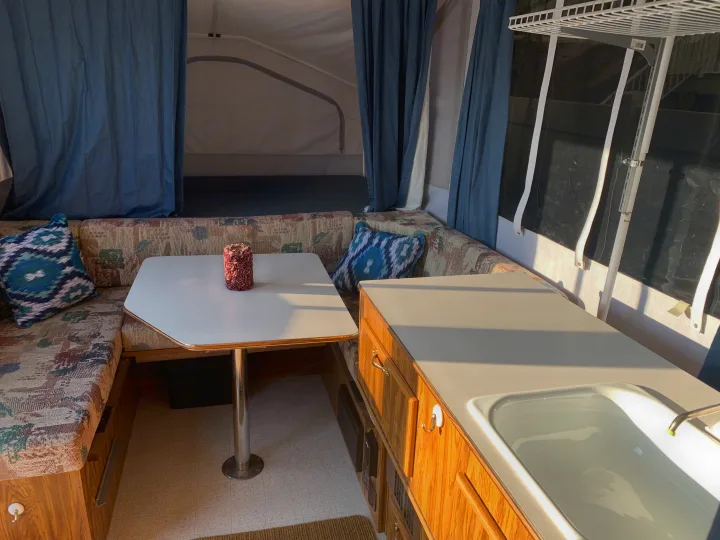 Cozy RV rental pop-up camper interior with a dining area, patterned cushions, and a compact kitchen sink.. Forest River Flagstaff 2000