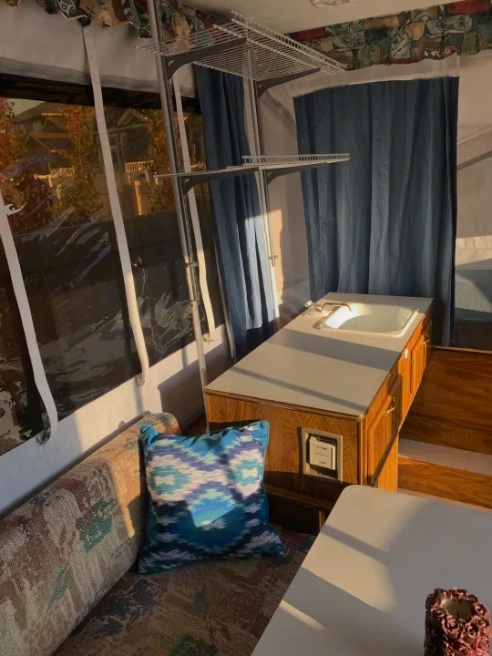Sunny pop-up camper RV rental interior with a sink, sofa, shelving, and window view of nature.. Forest River Flagstaff 2000