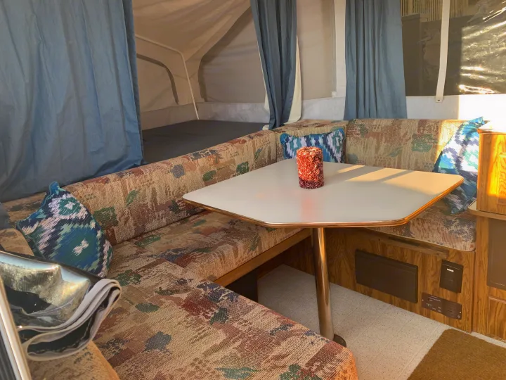Cozy RV rental dinette with patterned cushions and a central table, perfect for meals inside your pop-up camper.. Forest River Flagstaff 2000