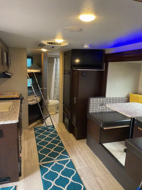 Bright rv rental interior with a kitchenette, bunk beds, dining area, and bathroom. Note the light decor and blue accent lighting.. Sportsmen Sportsmen Trailer 2017
