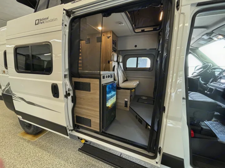 Open side door of a white camper van, showcasing its compact interior with a fridge and seating. Ideal for an rv rental adventure.. Winnebago Solis NPF 2025