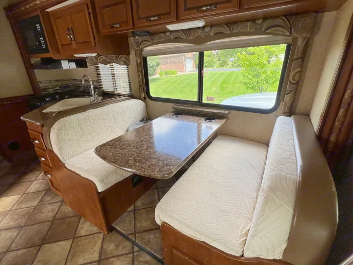 RV rental interior: bright dinette with patterned booth seating, speckled table, and a full kitchen area.. Thor Four Winds 2015