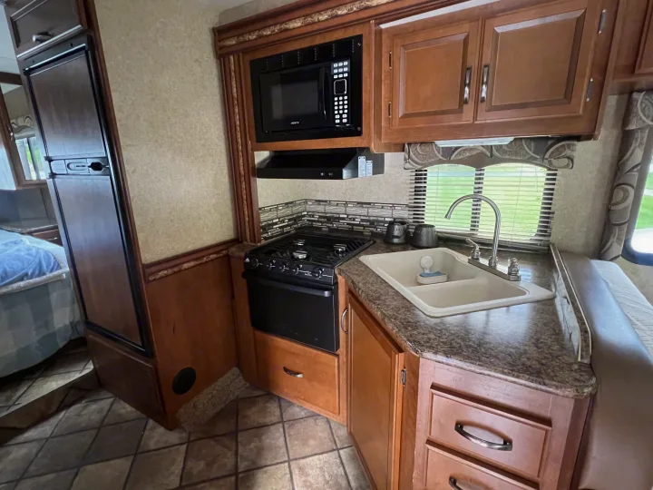 Inside an RV rental: a compact kitchen featuring a microwave, stove, fridge, and sink with ample cabinet space.. Thor Four Winds 2015