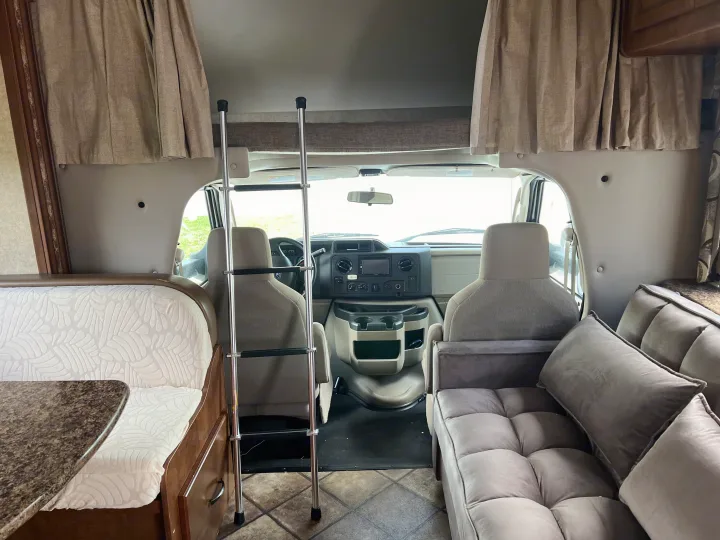 This RV rental interior showcases a cozy dinette, ladder to an over-cab bunk, front cabin, and comfortable sofa.. Thor Four Winds 2015