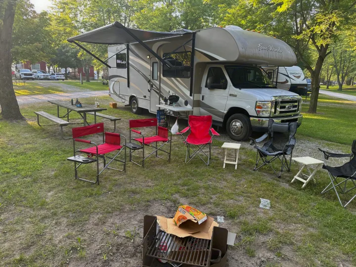 This RV rental campsite boasts an extended awning, multiple chairs, a picnic table, and a grill, ready for outdoor fun.. Thor Four Winds 2015