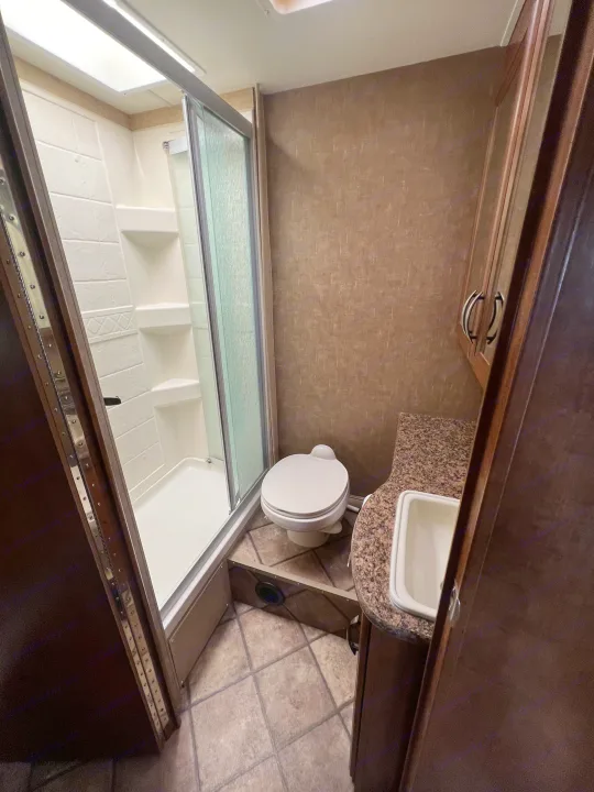 RV rental bathroom featuring a glass-enclosed shower, toilet, and vanity with sink. Practical for travel.. Thor Four Winds 2015