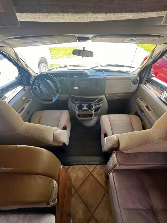 RV rental cockpit: view from behind light tan seats showing dashboard, steering wheel, and cupholders.. Thor Four Winds 2015