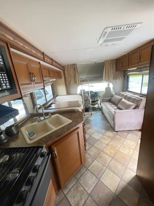 Explore this well-equipped RV rental interior: full kitchen, comfy living area, and overhead bunk for comfortable travel.. Thor Four Winds 2015