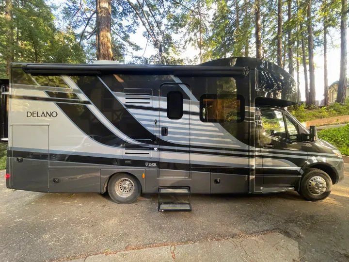 Thor Delano RV rental: a modern black and gray motorhome parked with steps extended, surrounded by tall trees.. Thor Delano Sprinter 2020