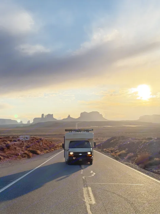 An RV rental on a long desert road at sunset, facing iconic Monument Valley formations, perfect for a scenic road trip.. Chevrolet Express 2011