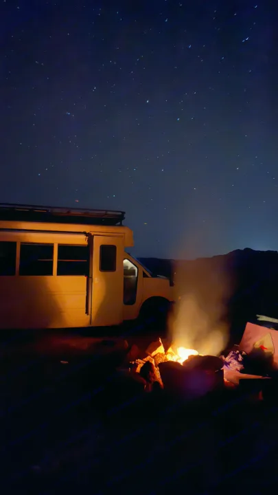 An RV rental parked under a clear, star-filled night sky, with a warm campfire burning brightly in the foreground.. Chevrolet Express 2011