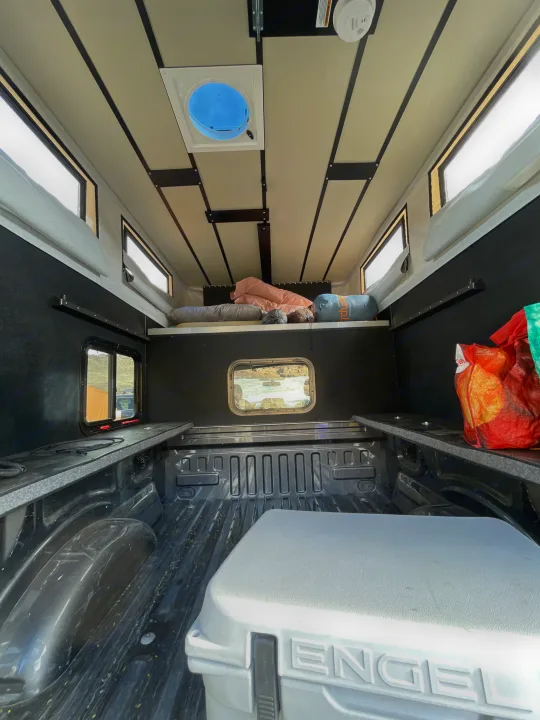 Inside an RV rental truck bed camper: A cozy sleeping platform, side storage, Engel cooler, windows, and roof vent are visible.. Four Wheel Campers Shell Models 2020