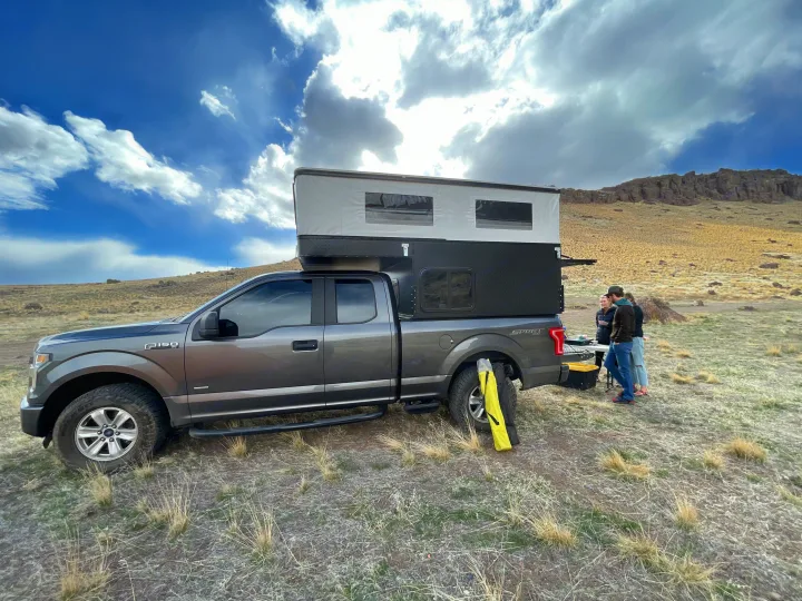 Grey Ford F-150 truck with a deployed pop-up RV rental camper. People gather by the back, camping in a desert.. Four Wheel Campers Shell Models 2020