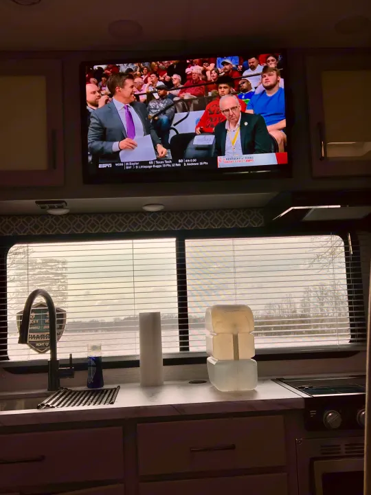 Enjoying an RV rental: a basketball game on TV, a functional kitchen, and a peaceful lake view through the blinds.. Thor Coleman 2024