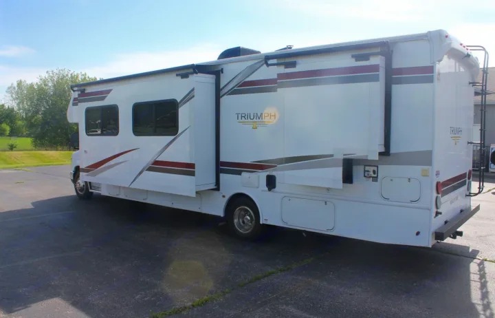 A white Triumph motorhome RV rental, with slide-outs extended, parked on asphalt under a blue sky.. Nexus RV Triumph 2021