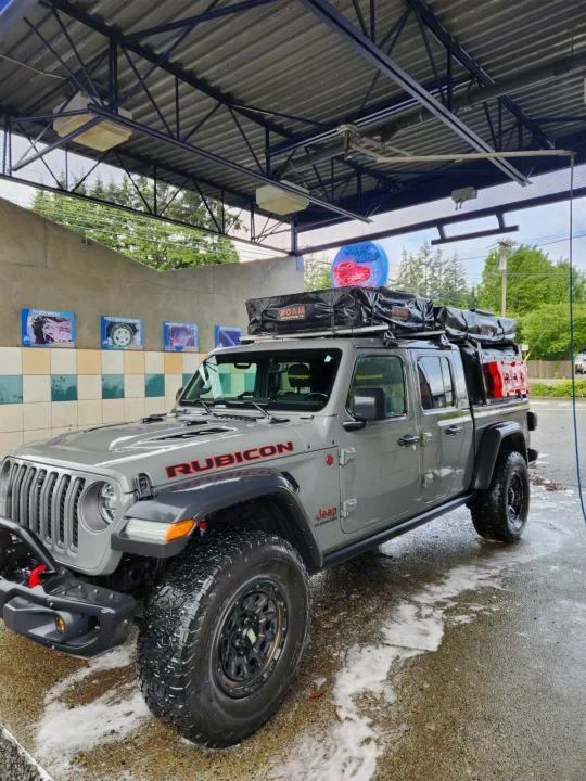 Grey Jeep Gladiator Rubicon with rooftop tent at a car wash. Perfect adventure rig, an exciting twist on rv rental camping!. Jeep Gladiator 2021