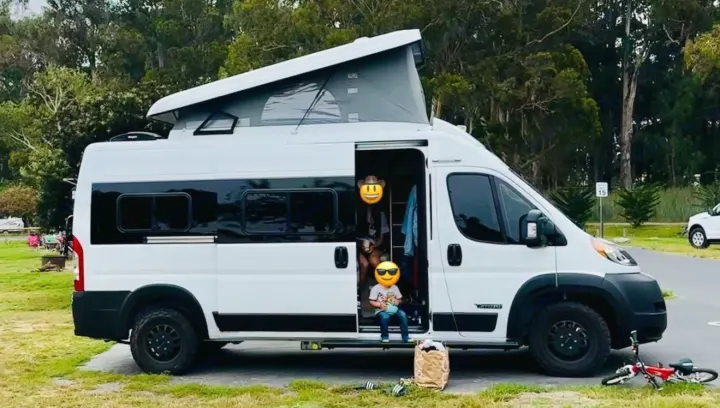 An rv rental white camper van with a pop-top roof at a green campsite, family outside enjoying the trip.. Winnebago Solis 2023