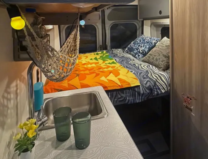 Cozy rv rental interior featuring a bed with vibrant bedding, a compact kitchen sink, and decorative hanging net lights.. Winnebago Solis 2023