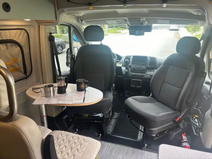 Cozy RV rental interior with front seats swiveled, table set for coffee & maps. Perfect for a road trip adventure!. Winnebago Solis 2023