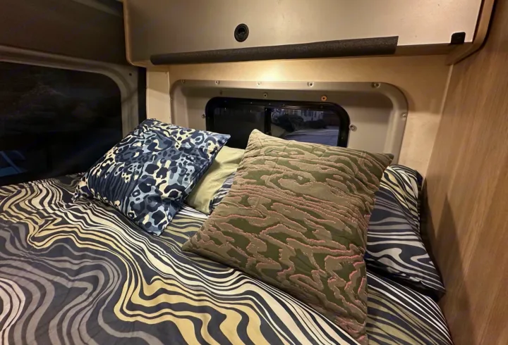 Inviting RV rental bed with playful patterned pillows and bedding in a compact, cozy interior. Perfect for travel.. Winnebago Solis 2023