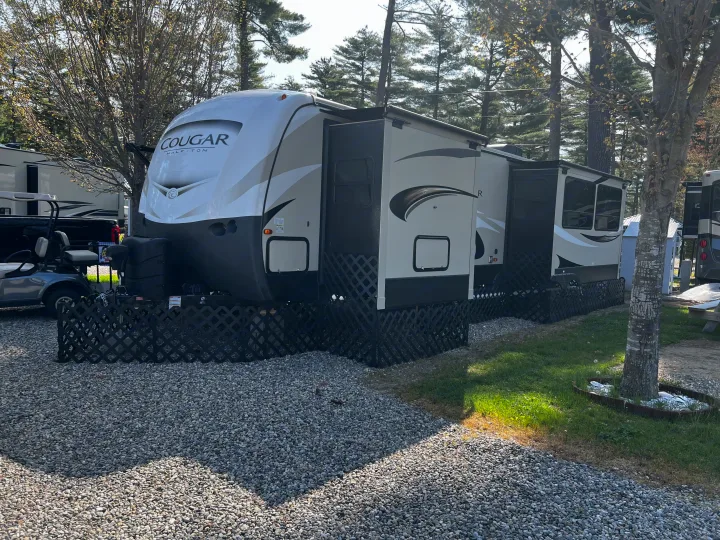 Spacious Cougar Half-Ton RV rental parked at a sunny campground site, with slide-outs extended, skirting, and a golf cart.. Keystone RV Cougar X-Lite 2018