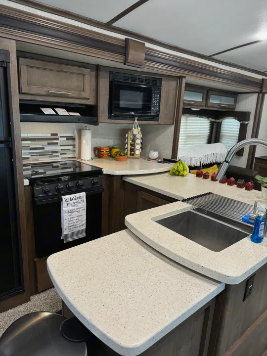 Modern RV rental kitchen: dark wood cabinets, light speckled counters, stove, microwave, sink, and ample counter space.. Keystone RV Cougar X-Lite 2018