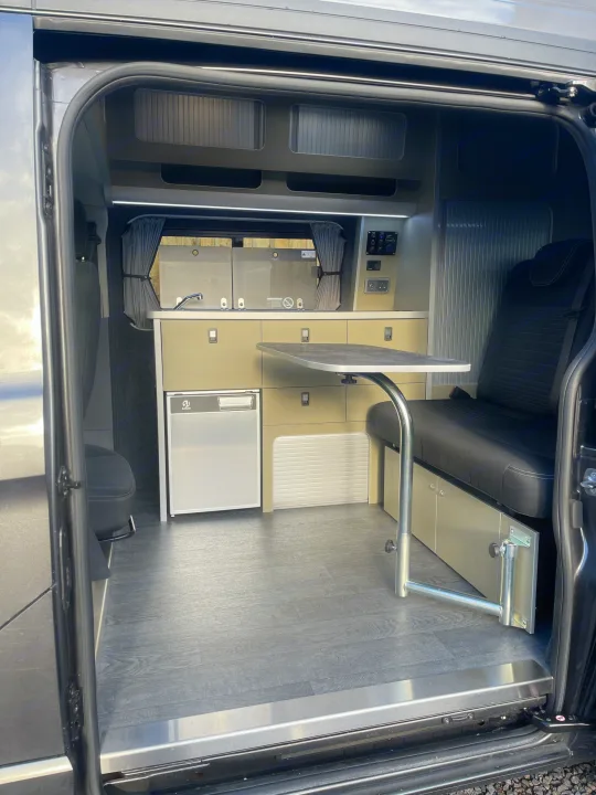 Inside a sleek RV rental, this modern camper van conversion offers a kitchen, dining table, and comfy bench seating.. Ford Transit Custom 2 berth Hi-line Automatic 2021