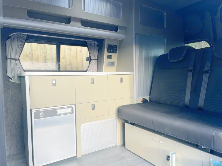 Explore this RV rental's well-designed interior, featuring a compact kitchen with a Sanjo fridge, storage, and bench seating.. Ford Transit Custom 2 berth Hi-line Automatic 2021