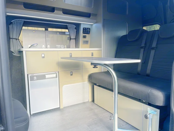 RV rental interior: modern campervan setup featuring a kitchen, adjustable table, and rear passenger seats.. Ford Transit Custom 2 berth Hi-line Automatic 2021