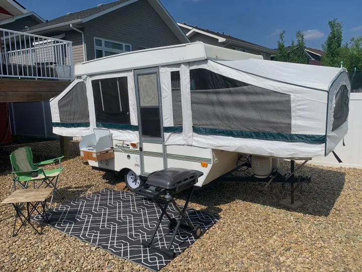 Pop-up Palomino camper set up in a gravel yard, perfect for an RV rental adventure. Includes outdoor grill & seating.. Forest River Palomino 2003