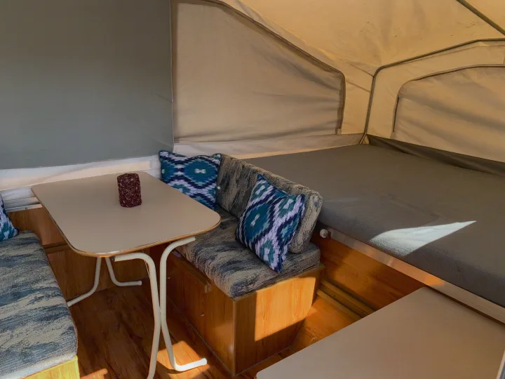 Cozy RV rental interior with a table, padded benches, and a sleeping area. Sunlit space for comfortable travel.. Forest River Palomino 2003