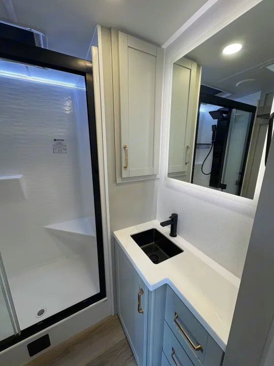 Sleek RV rental bathroom with a black-framed shower (still wrapped in plastic), modern vanity, black sink, and lit mirror.. Brinkley 295 AIR 2025