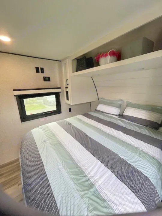 Cozy RV rental bedroom with striped bedding, a window, and overhead storage. A well-organized space for your next adventure.. Jayco Jay Flight 2024