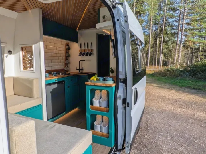 Step into this bright rv rental camper van: modern teal kitchen, comfy beige seating, wood accents, and a tranquil forest view awaits.. Peugeot Boxer L4H2 2021