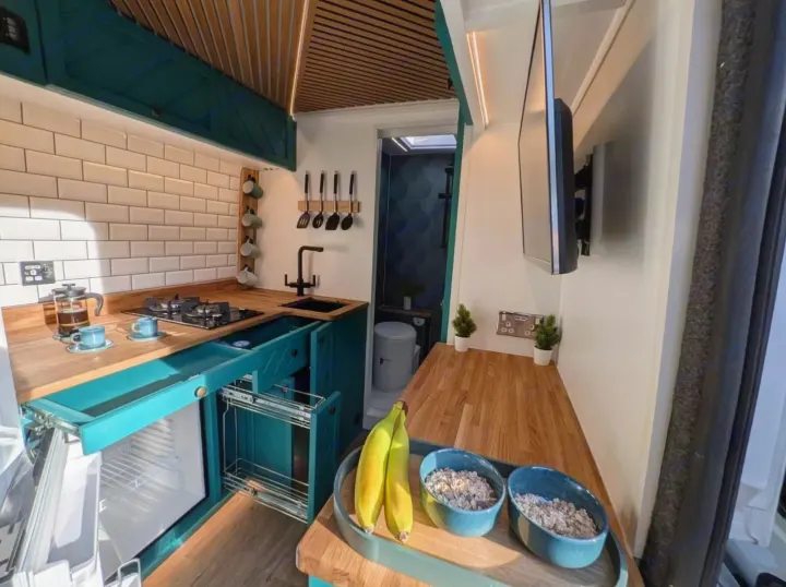 Tour this modern RV rental's clever interior: a teal kitchen with a stove, sink, fridge, TV, and a glimpse of the shower.. Peugeot Boxer L4H2 2021