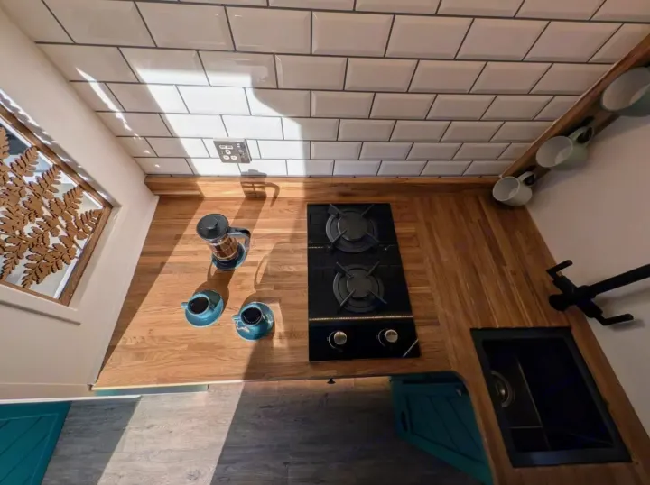 Overhead view of an RV rental's modern compact kitchen. Shows white subway tiles, wood counter, stove, sink, and coffee accessories.. Peugeot Boxer L4H2 2021