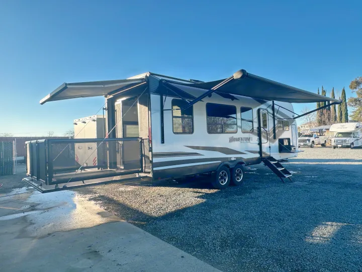 Spacious toy hauler RV rental with extended awnings and rear patio deck, ready for adventure on a sunny day.. Grand Design Momentum 2022